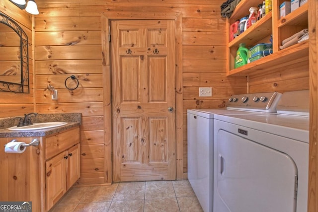 laundry area with wood walls, washer and clothes dryer, light tile patterned flooring, and a sink