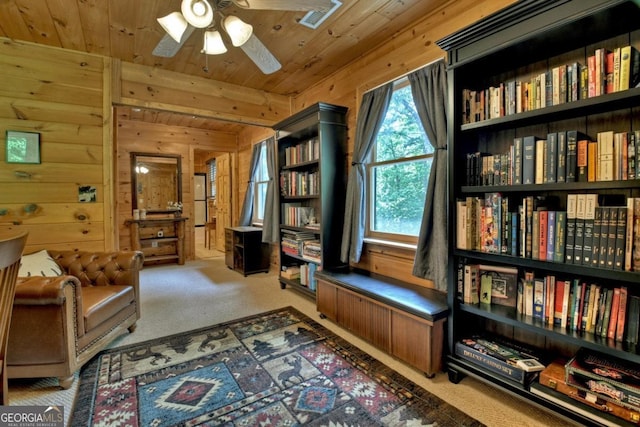 sitting room featuring wood walls, carpet, wooden ceiling, and a ceiling fan