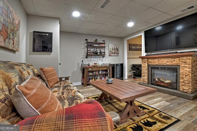 living room featuring a paneled ceiling, a fireplace, wood finished floors, and visible vents