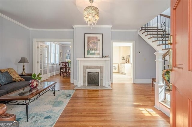 living room featuring baseboards, a tiled fireplace, ornamental molding, stairs, and light wood-style floors