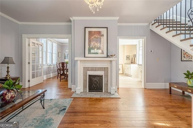 living area featuring ornamental molding, a tile fireplace, wood-type flooring, and stairs