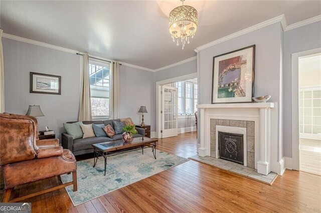 living room featuring a chandelier, hardwood / wood-style flooring, a fireplace, baseboards, and crown molding