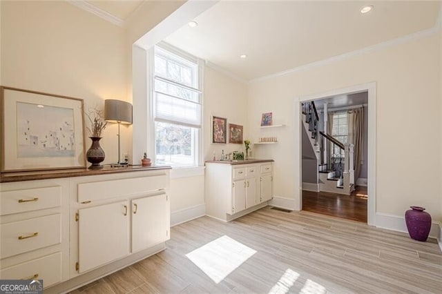 bar with light wood finished floors, baseboards, stairs, and ornamental molding