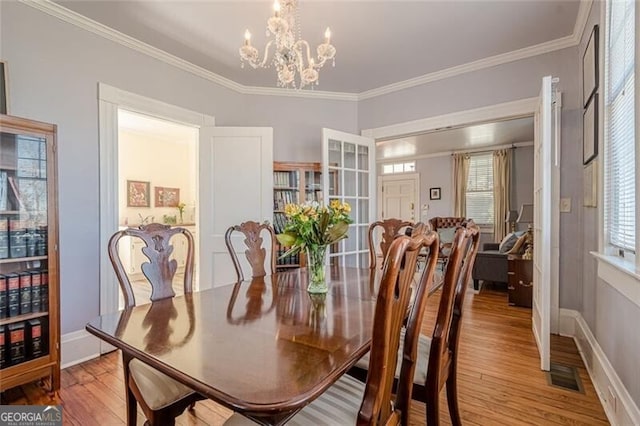 dining space featuring light wood finished floors, a notable chandelier, visible vents, and crown molding