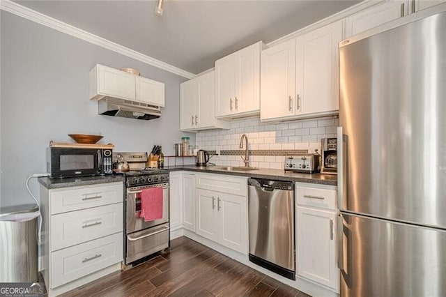 kitchen with dark countertops, stainless steel appliances, crown molding, under cabinet range hood, and a sink