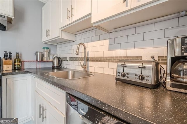 kitchen with dark countertops, white cabinetry, a sink, and backsplash