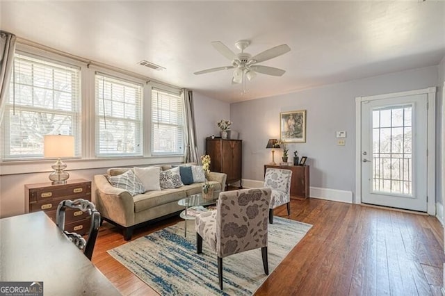 living area featuring wood-type flooring, visible vents, ceiling fan, and baseboards