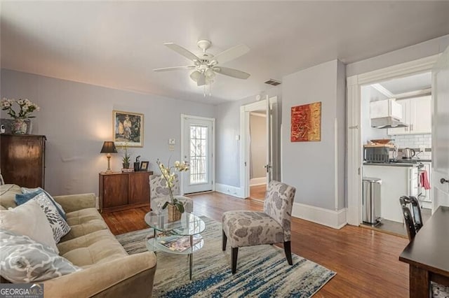 living room with a ceiling fan, visible vents, baseboards, and wood finished floors