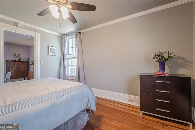 bedroom featuring a ceiling fan, baseboards, crown molding, and wood finished floors