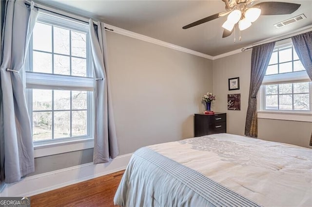 bedroom with dark wood-style floors, crown molding, visible vents, a ceiling fan, and baseboards