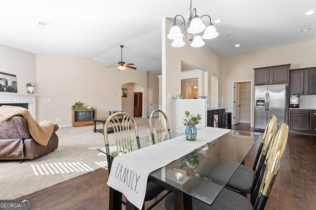 dining area with arched walkways, recessed lighting, a fireplace, vaulted ceiling, and dark wood finished floors