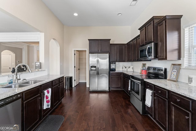 kitchen featuring arched walkways, light stone counters, stainless steel appliances, and a sink