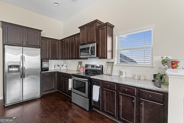 kitchen featuring dark brown cabinetry, dark wood-style flooring, light stone countertops, stainless steel appliances, and backsplash