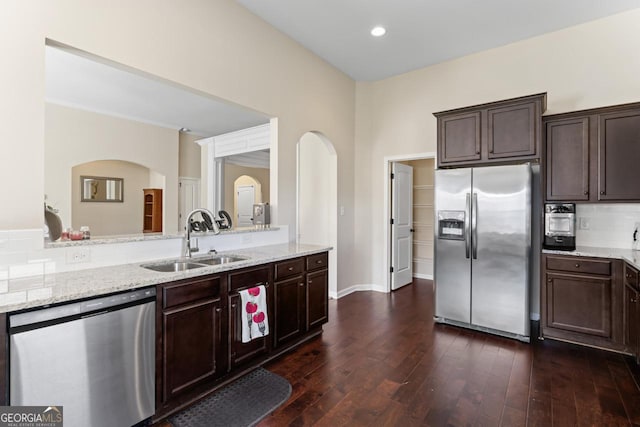 kitchen featuring stainless steel appliances, a sink, dark brown cabinets, light stone countertops, and dark wood finished floors