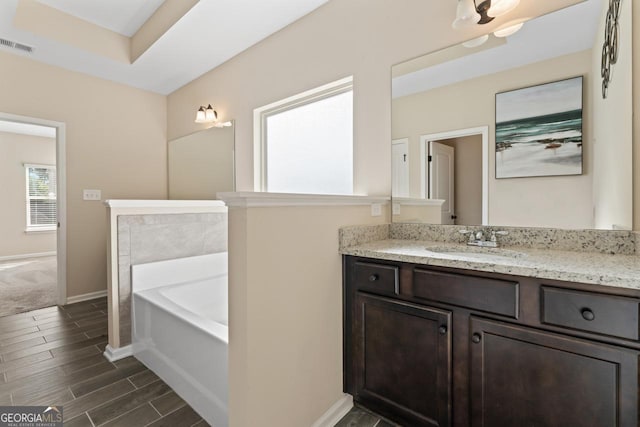 bathroom featuring baseboards, visible vents, vanity, wood finish floors, and a bath