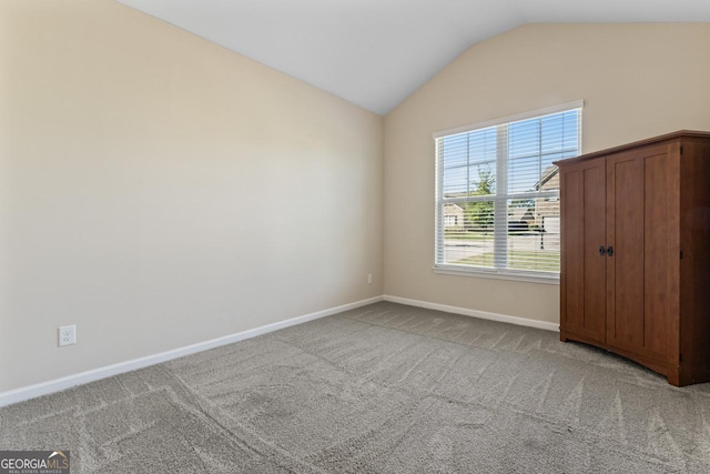 empty room featuring carpet flooring, vaulted ceiling, and baseboards