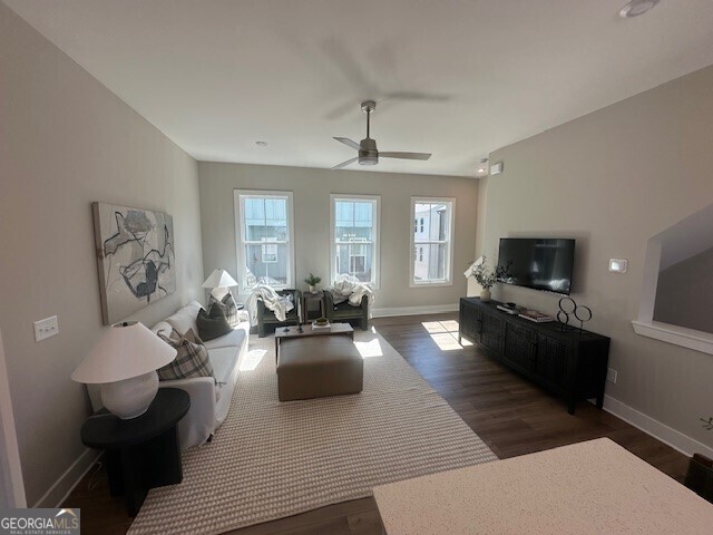 living area with dark wood-type flooring, a ceiling fan, and baseboards