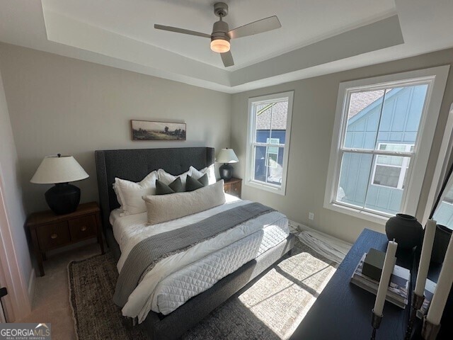 carpeted bedroom featuring a raised ceiling and ceiling fan