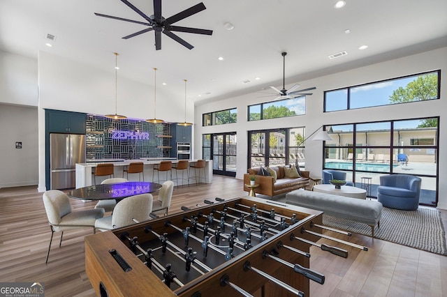 recreation room with french doors, a healthy amount of sunlight, light wood-style flooring, and a high ceiling