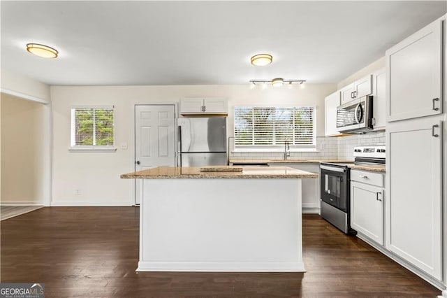 kitchen with light stone counters, stainless steel appliances, a kitchen island, tasteful backsplash, and dark wood finished floors