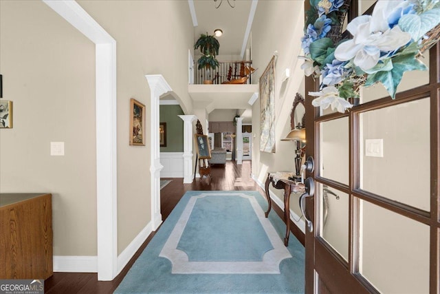 corridor featuring arched walkways, wood finished floors, a towering ceiling, stairway, and decorative columns