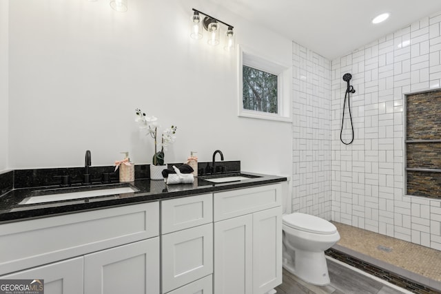 full bathroom featuring double vanity, tiled shower, a sink, and toilet