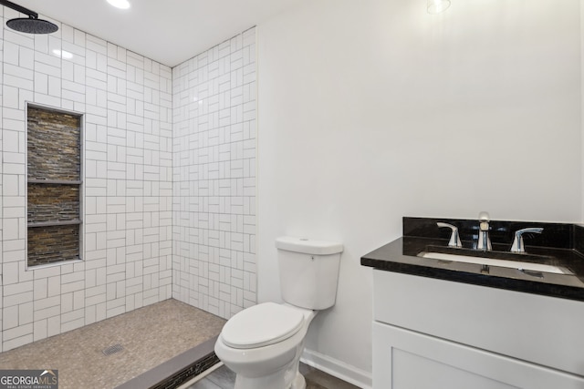 bathroom featuring baseboards, tiled shower, vanity, and toilet