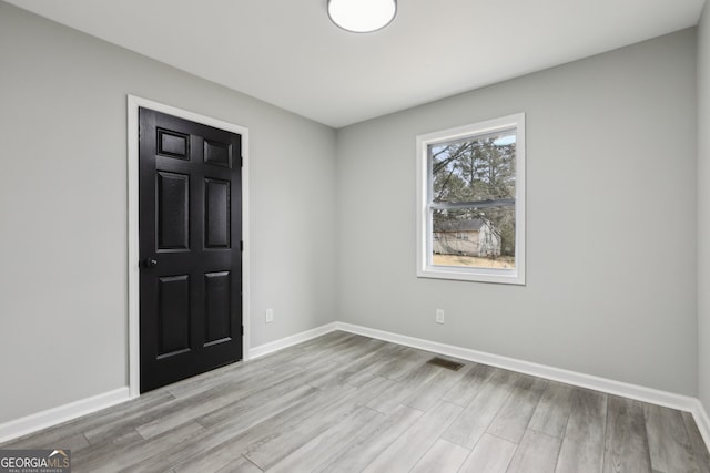 empty room featuring light wood-type flooring, visible vents, and baseboards