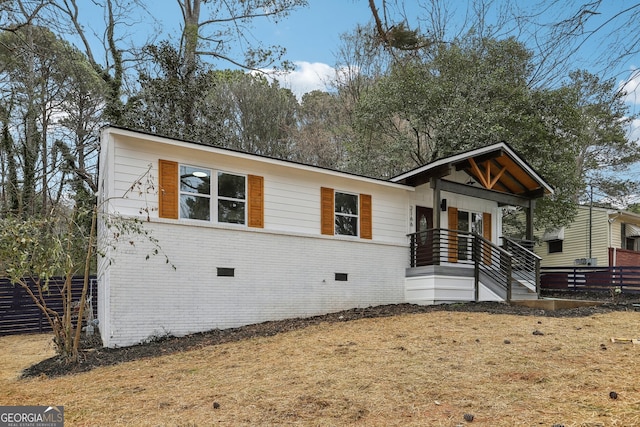 view of front of house featuring crawl space, brick siding, and fence