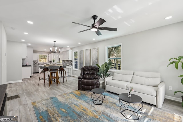 living room with ceiling fan with notable chandelier, light wood-type flooring, and recessed lighting