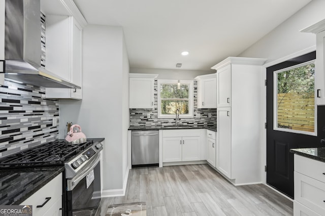 kitchen with stainless steel appliances, wall chimney exhaust hood, a sink, and white cabinetry