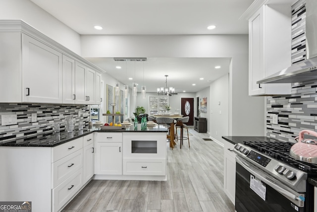 kitchen with light wood-style flooring, a peninsula, wall chimney range hood, white cabinetry, and gas stove