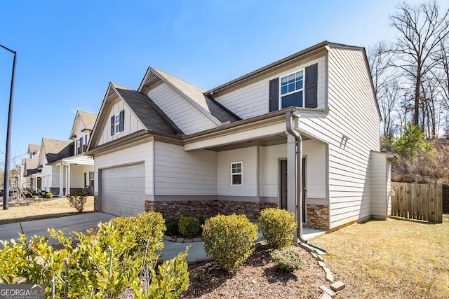 view of front of property featuring fence, driveway, a garage, stone siding, and board and batten siding