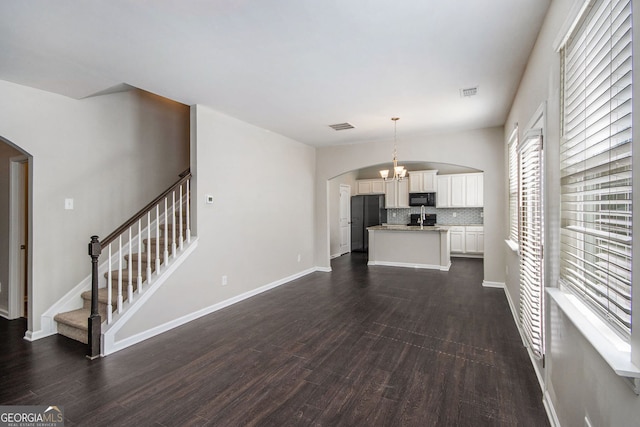 unfurnished living room featuring visible vents, dark wood finished floors, stairway, arched walkways, and a chandelier