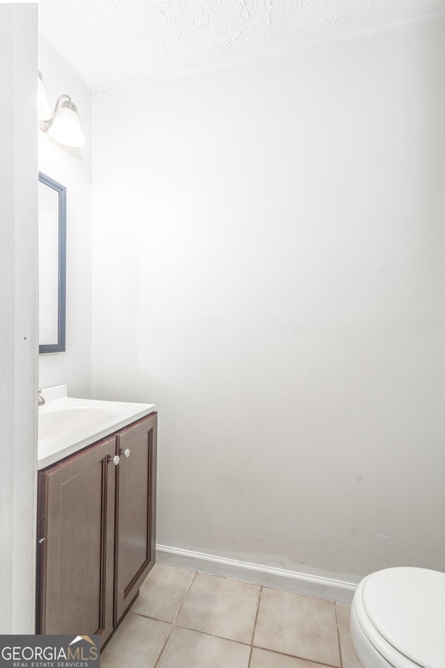 half bath with tile patterned flooring, toilet, vanity, and baseboards