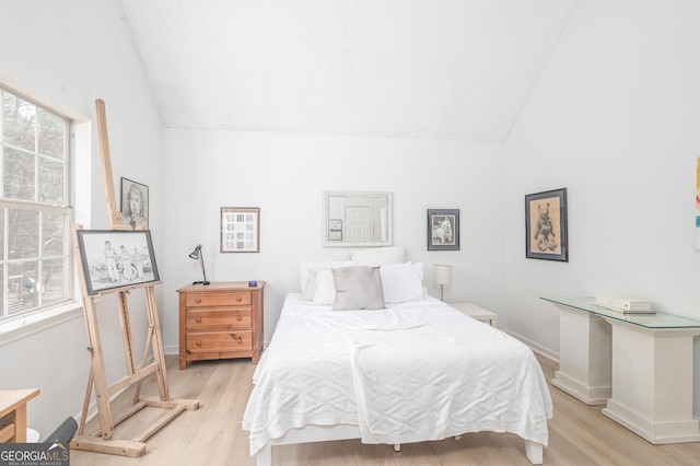 bedroom featuring vaulted ceiling, multiple windows, and light wood-style flooring