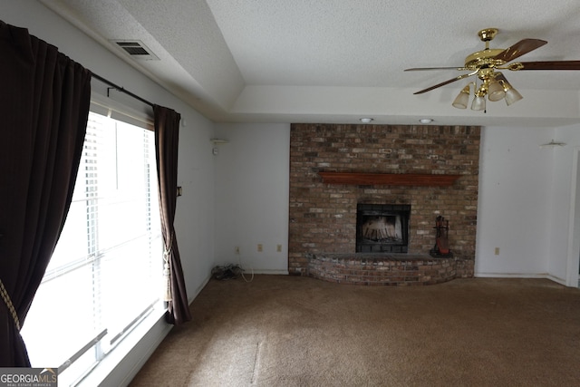 unfurnished living room featuring visible vents, ceiling fan, a textured ceiling, carpet flooring, and a brick fireplace