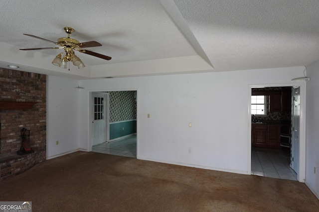 unfurnished living room featuring a textured ceiling, a tray ceiling, light tile patterned flooring, and light colored carpet