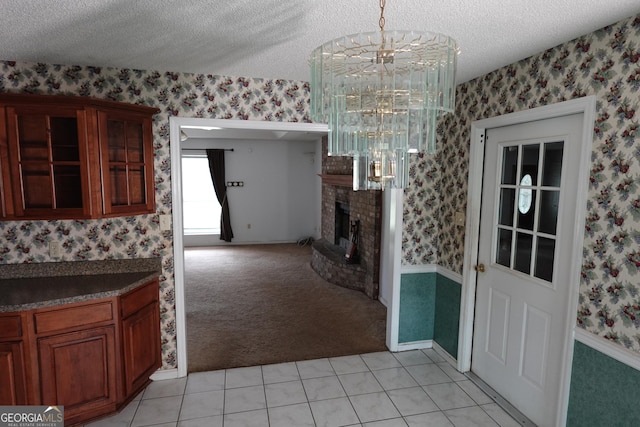 unfurnished dining area featuring a textured ceiling, light tile patterned floors, light colored carpet, a fireplace, and wallpapered walls