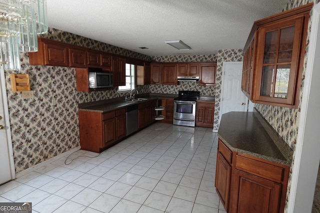 kitchen with appliances with stainless steel finishes, dark countertops, a textured ceiling, and wallpapered walls