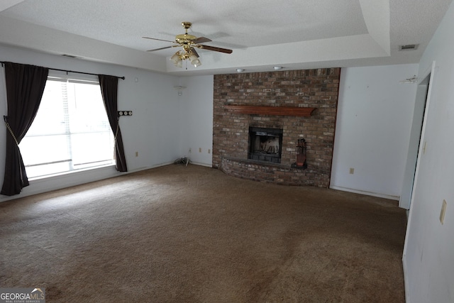 unfurnished living room with a brick fireplace, carpet, a raised ceiling, and a textured ceiling