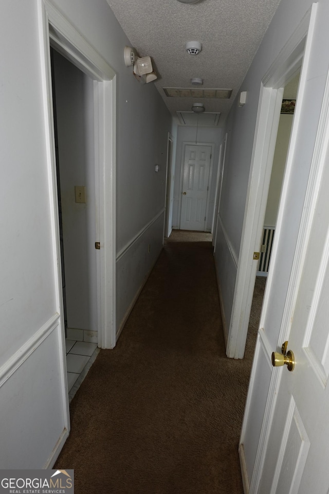 corridor featuring attic access, carpet, and a textured ceiling