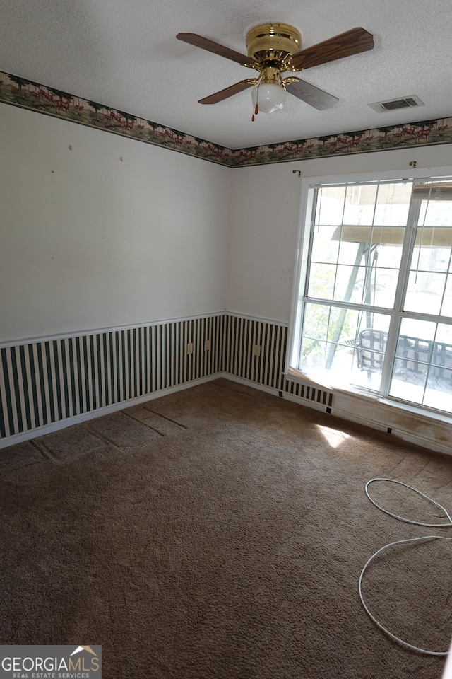 carpeted empty room with a textured ceiling, visible vents, and a ceiling fan