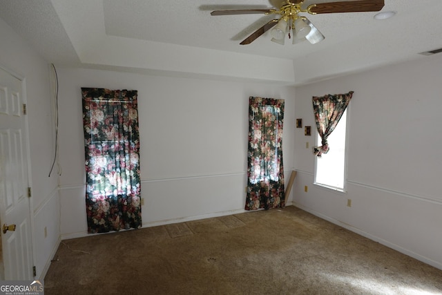 carpeted empty room featuring a textured ceiling, a tray ceiling, visible vents, and a ceiling fan