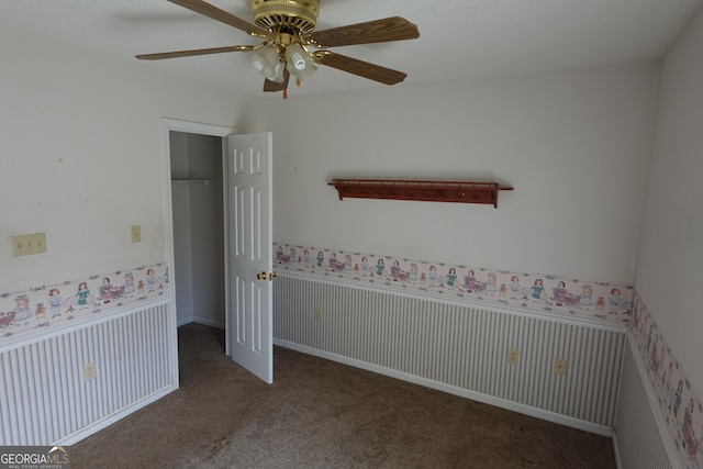 empty room with carpet floors, a wainscoted wall, wallpapered walls, and a ceiling fan