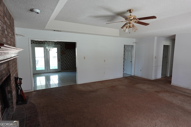 unfurnished living room with a textured ceiling, a tray ceiling, carpet, and a brick fireplace