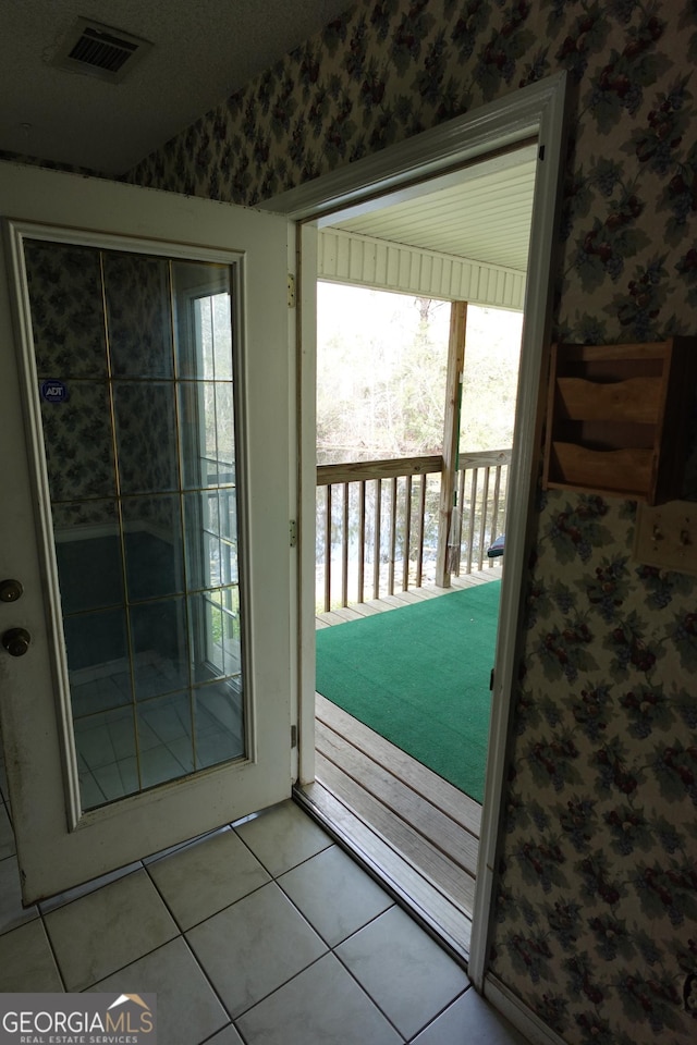 doorway to outside featuring tile patterned floors, visible vents, and wallpapered walls