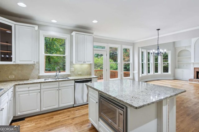 kitchen featuring light wood finished floors, stainless steel appliances, crown molding, a fireplace, and a sink