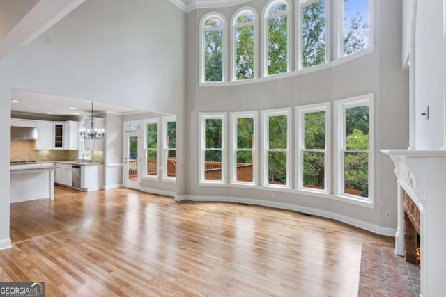 unfurnished living room with a towering ceiling, a brick fireplace, light wood finished floors, and a notable chandelier