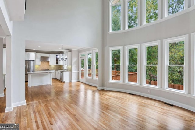 unfurnished living room with light wood-type flooring, a wealth of natural light, visible vents, and a notable chandelier